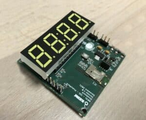 Carte électronique verte de 8cm x 5cm conçue sur mesure par BLUEGRioT pour un banc de test destiné à Decathlon. La carte présente une sérigraphie blanche, des composants variés, et un afficheur 7 segments à 4 digits
